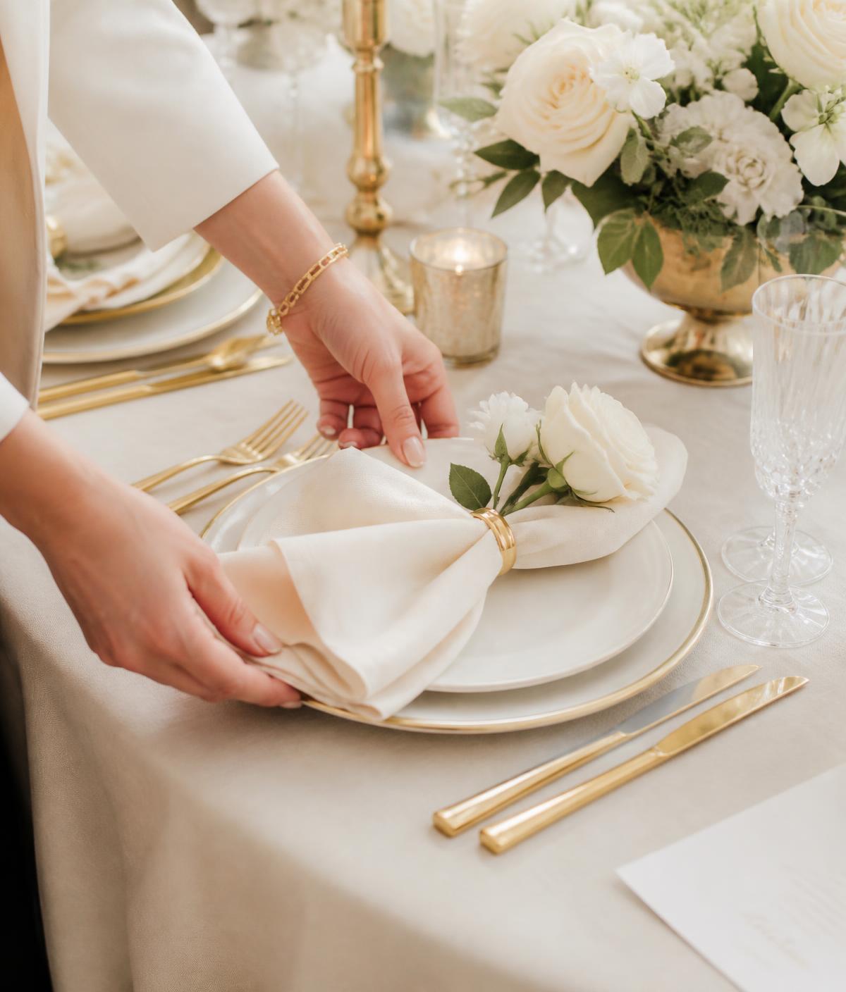 Stylist arranging an ivory and gold place setting with white roses